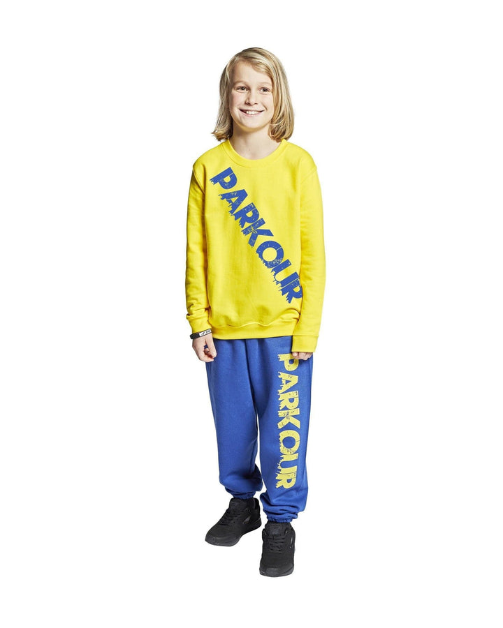 Malli keltaisessa ja sinisessä parkourasussa, johon kuuluu collegepaita ja housut.