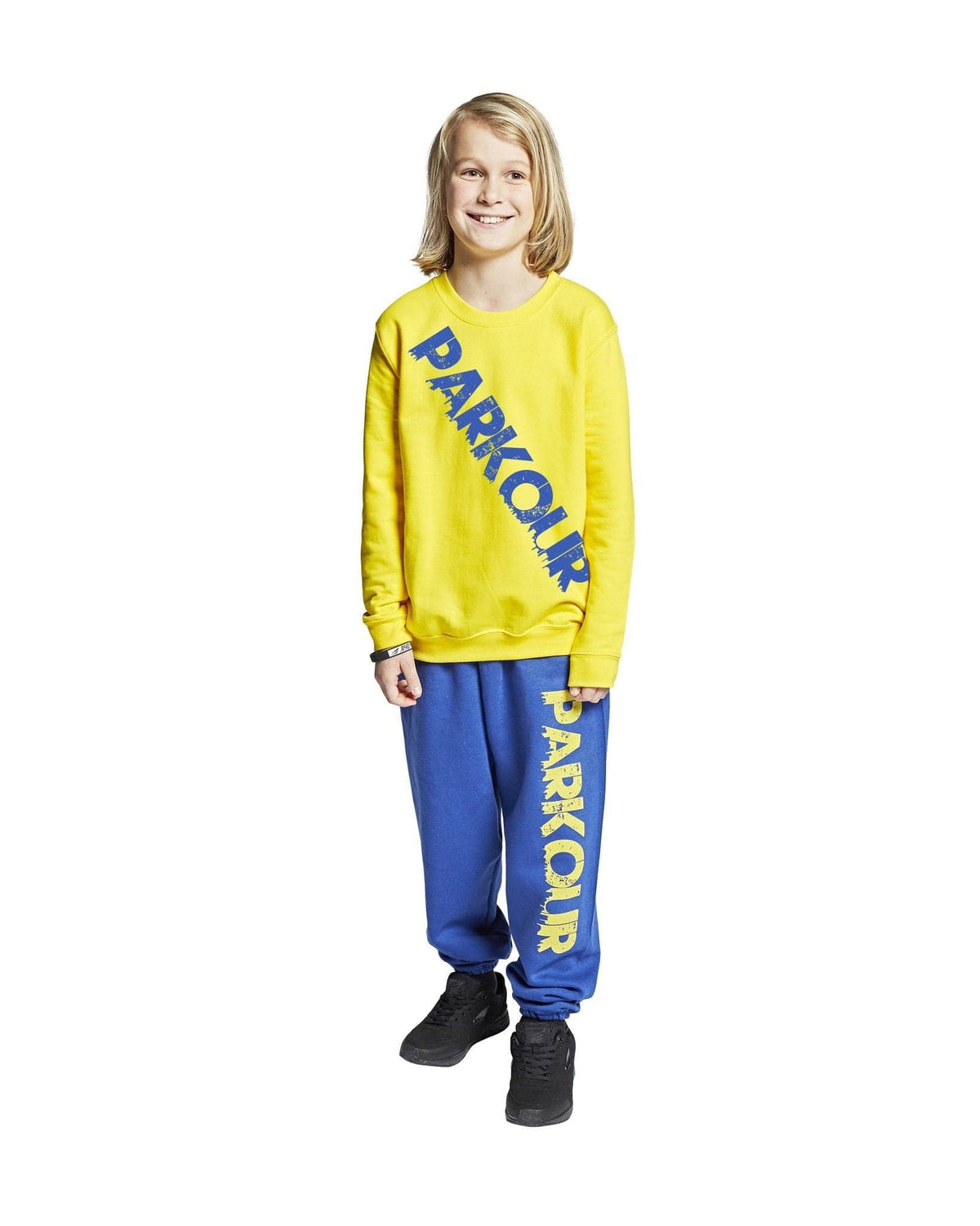 Malli keltaisessa ja sinisessä parkourasussa, johon kuuluu collegepaita ja housut.