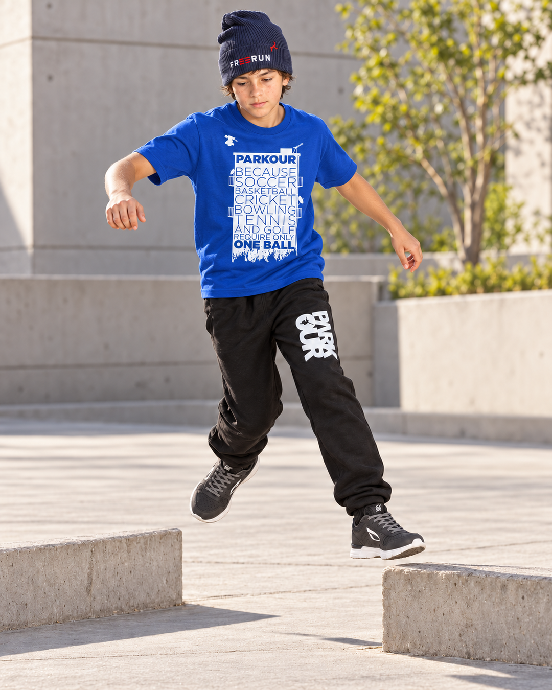 Blå Parkour Takes BALLS T-shirt med sorte/hvide bukser og navy FREERUN-hue – under træning. Sko købes separat.