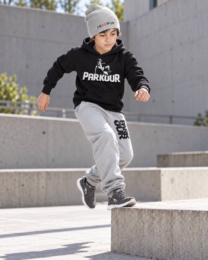 Sort Traceur-hoodie, grå/sorte bukser og grå FREERUN-hue – under parkourtræning.