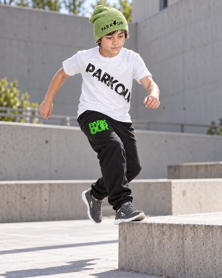 Hvid Urban Parkour T-shirt med sort diagonalt tryk, sorte/grønne bukser og grøn hue – i brug. Sko købes separat.