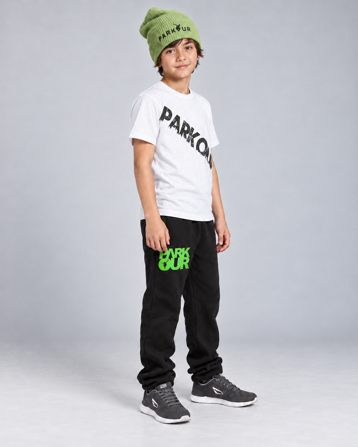 Hvid Urban Parkour T-shirt med sort diagonalt tryk, sorte/grønne bukser og grøn hue – fra siden.
