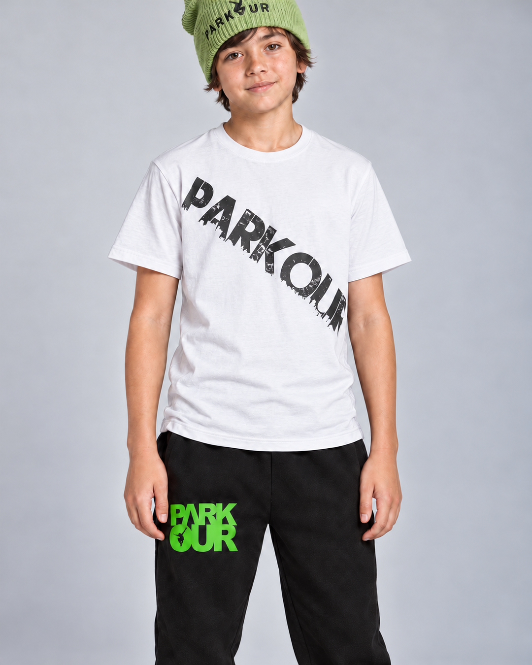 Hvid Urban Parkour T-shirt med sort diagonalt tryk, sorte/grønne bukser og grøn hue – detalje. Sko købes separat.