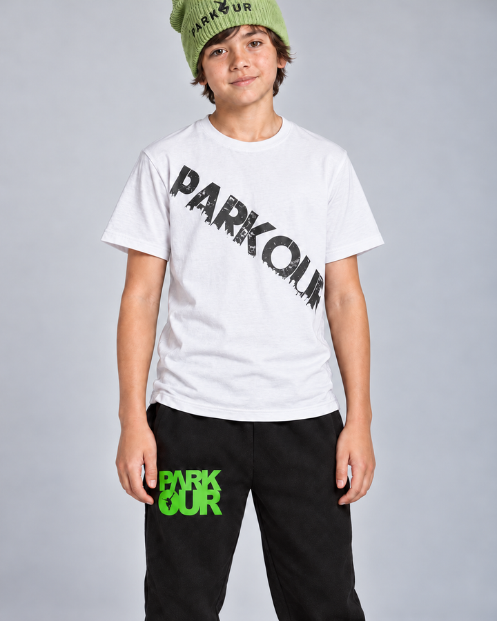 Hvid Urban Parkour T-shirt med sort diagonalt tryk, sorte/grønne bukser og grøn hue – detalje. Sko købes separat.