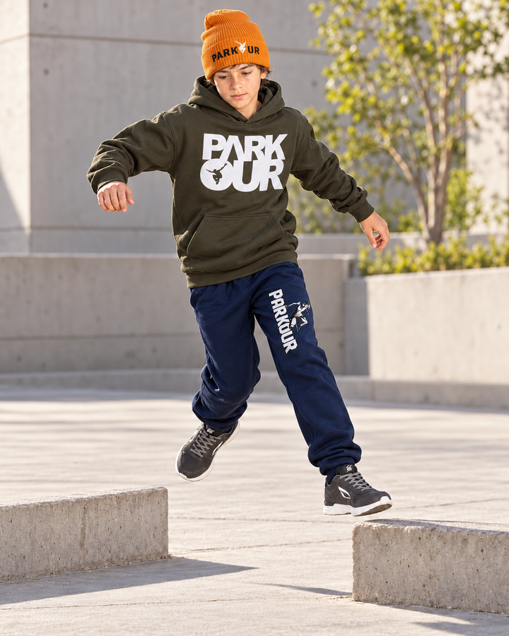 Oliven Parkour-hoodie, navy Traceur-bukser og orange Parkour-hue – under parkourtræning.