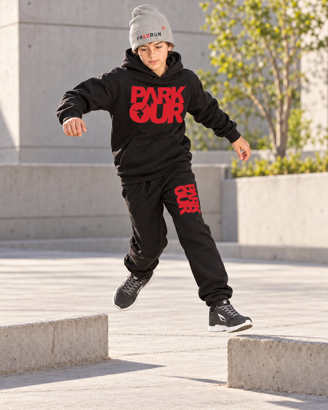 Sort/rød Parkour-hoodie og bukser med grå FREERUN-hue – under parkourtræning – fra Medium sort/rød. Sko købes separat.