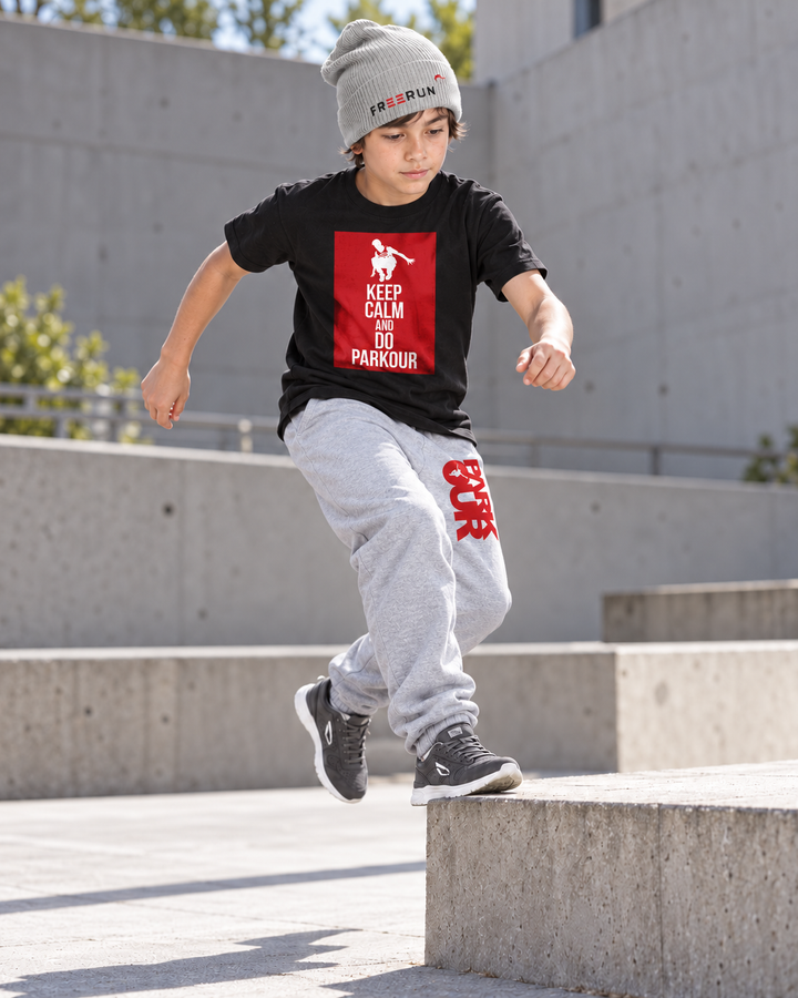 Sort Keep Calm T-shirt og grå/røde bukser med grå FREERUN-hue – under parkourtræning. Sko købes separat.