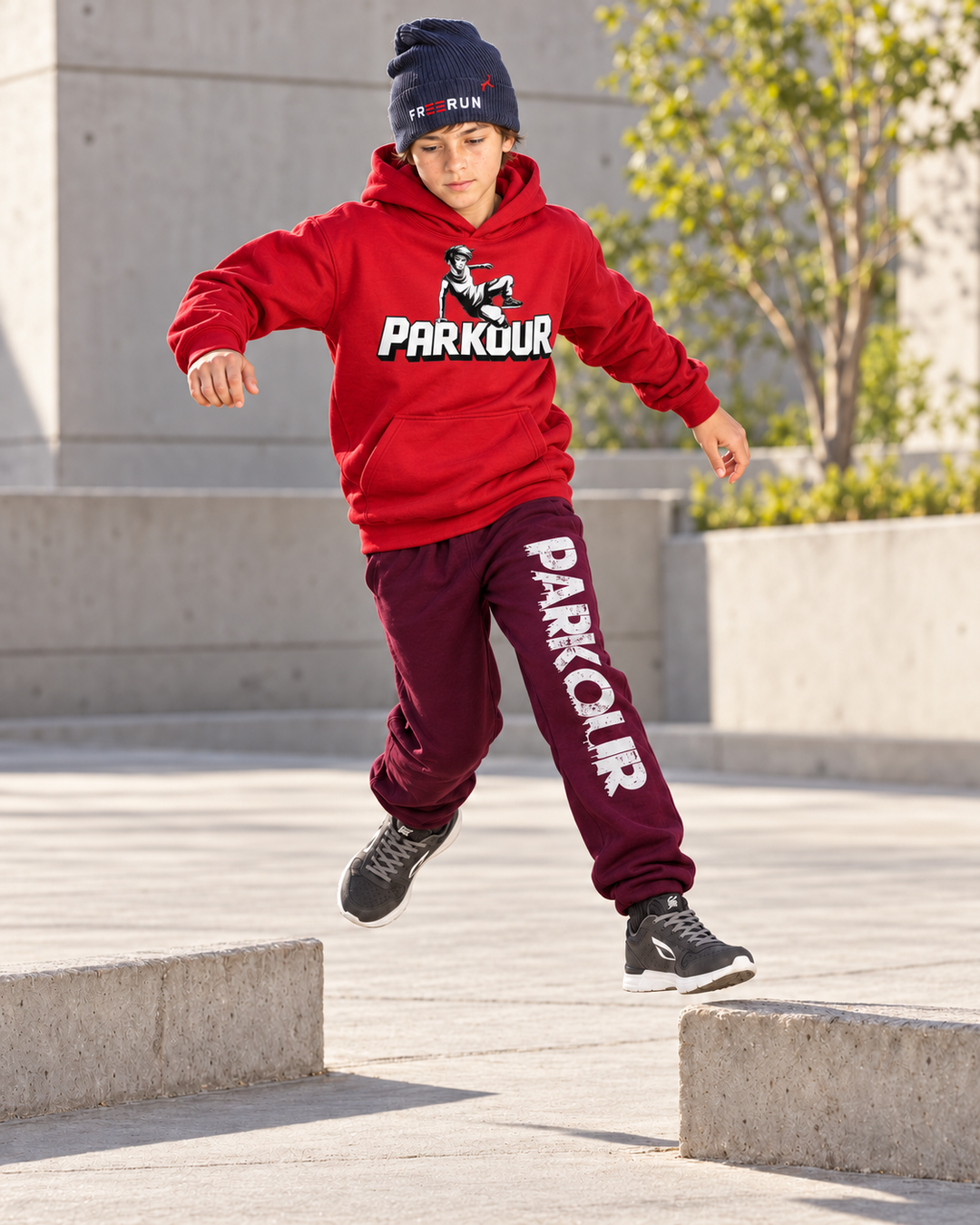 Rød Traceur-hoodie og bordeaux bukser med lodret Parkour-tryk – under parkourtræning.