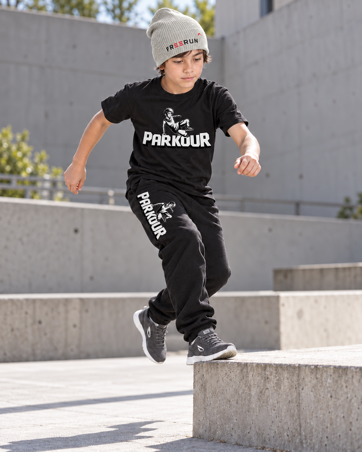 Traceur T-shirt og sorte Traceur-bukser med grå FREERUN-hue – under parkourtræning.