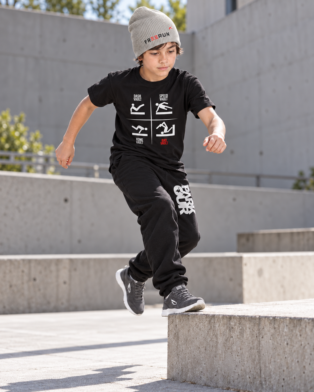 Sort VAULTS T-shirt med sorte/hvide bukser og grå FREERUN-hue – under parkourtræning. Sko købes separat.