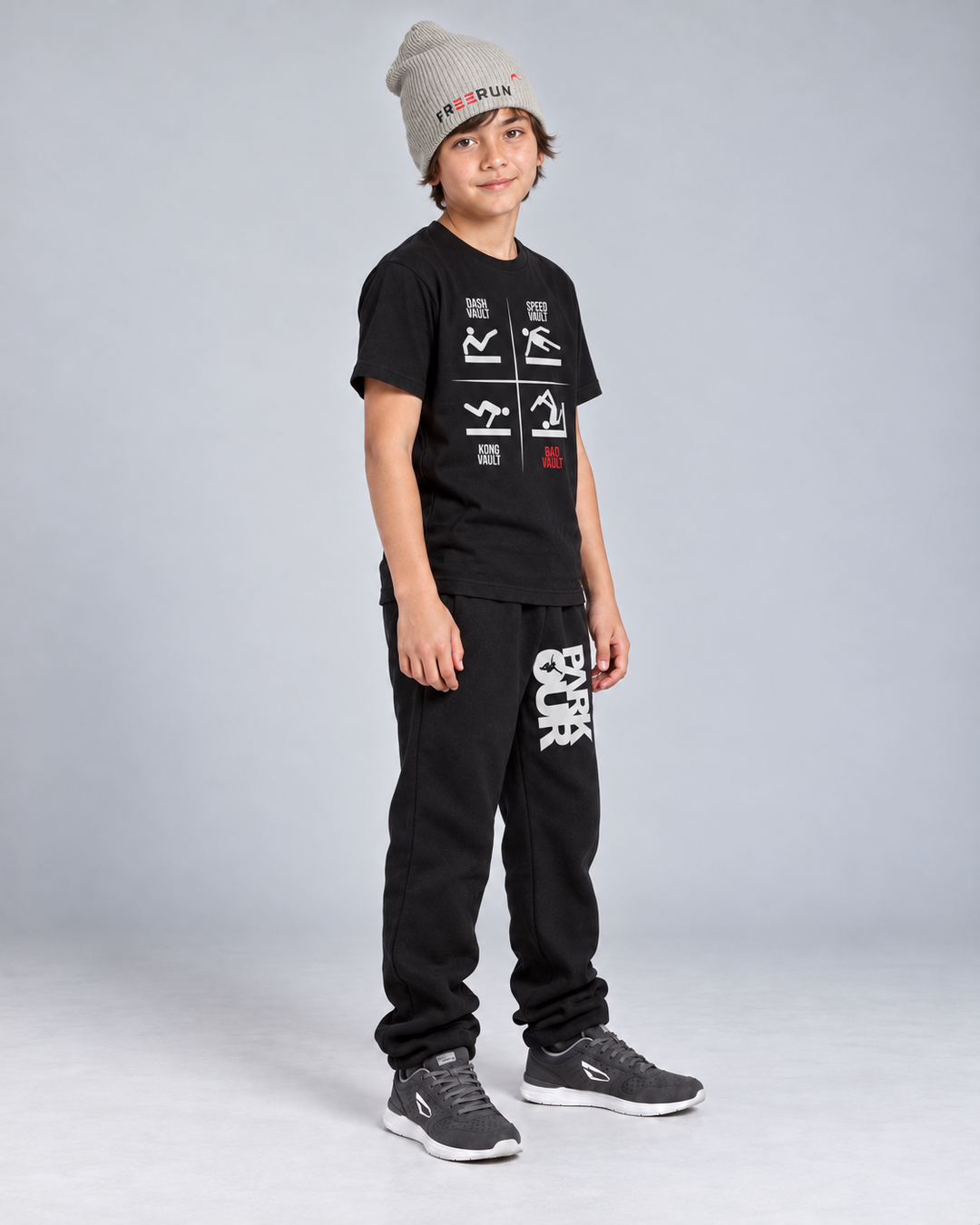 Sort VAULTS T-shirt med sorte/hvide bukser og grå FREERUN-hue – fra siden. Sko købes separat.