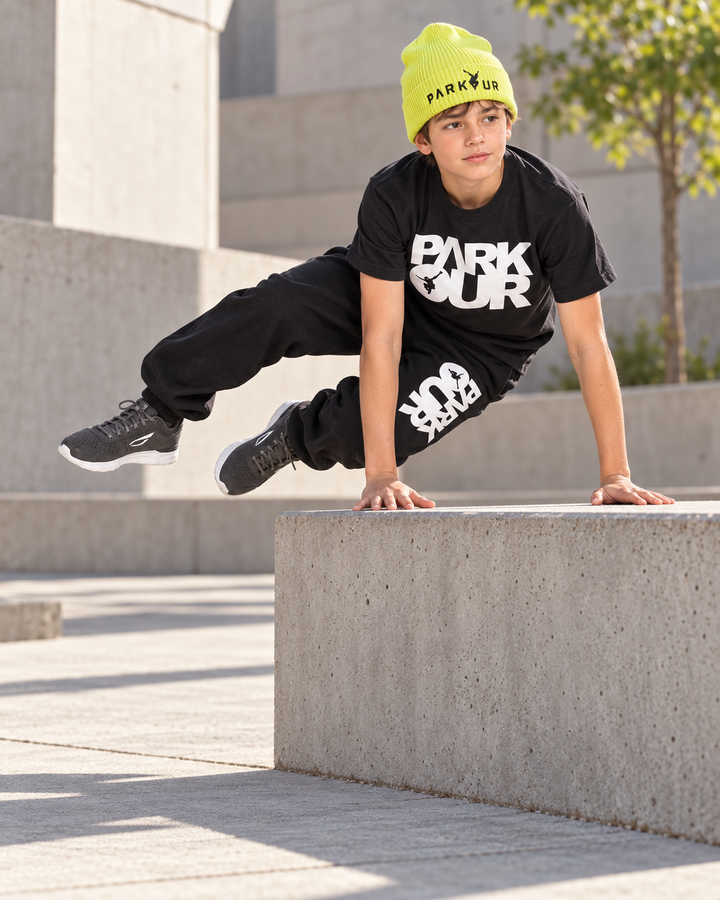 Dreng i sort/hvidt Parkour-outfit, gul hue og JIYO Flow 2.0 ved lavt parkour-vault